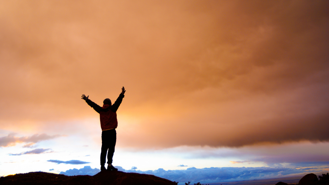 Person with arms raised against a dramatic sunset sky